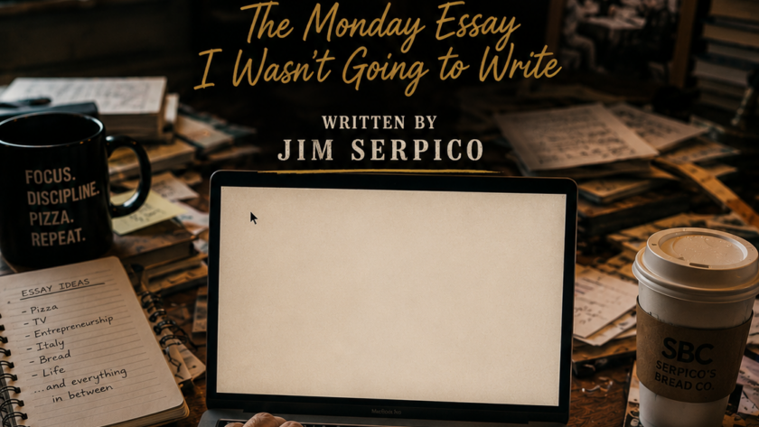 Over-the-shoulder view of hands typing on a laptop at a cluttered desk with notes, coffee cup, and a large 'MONDAY ESSAY' poster in the background.